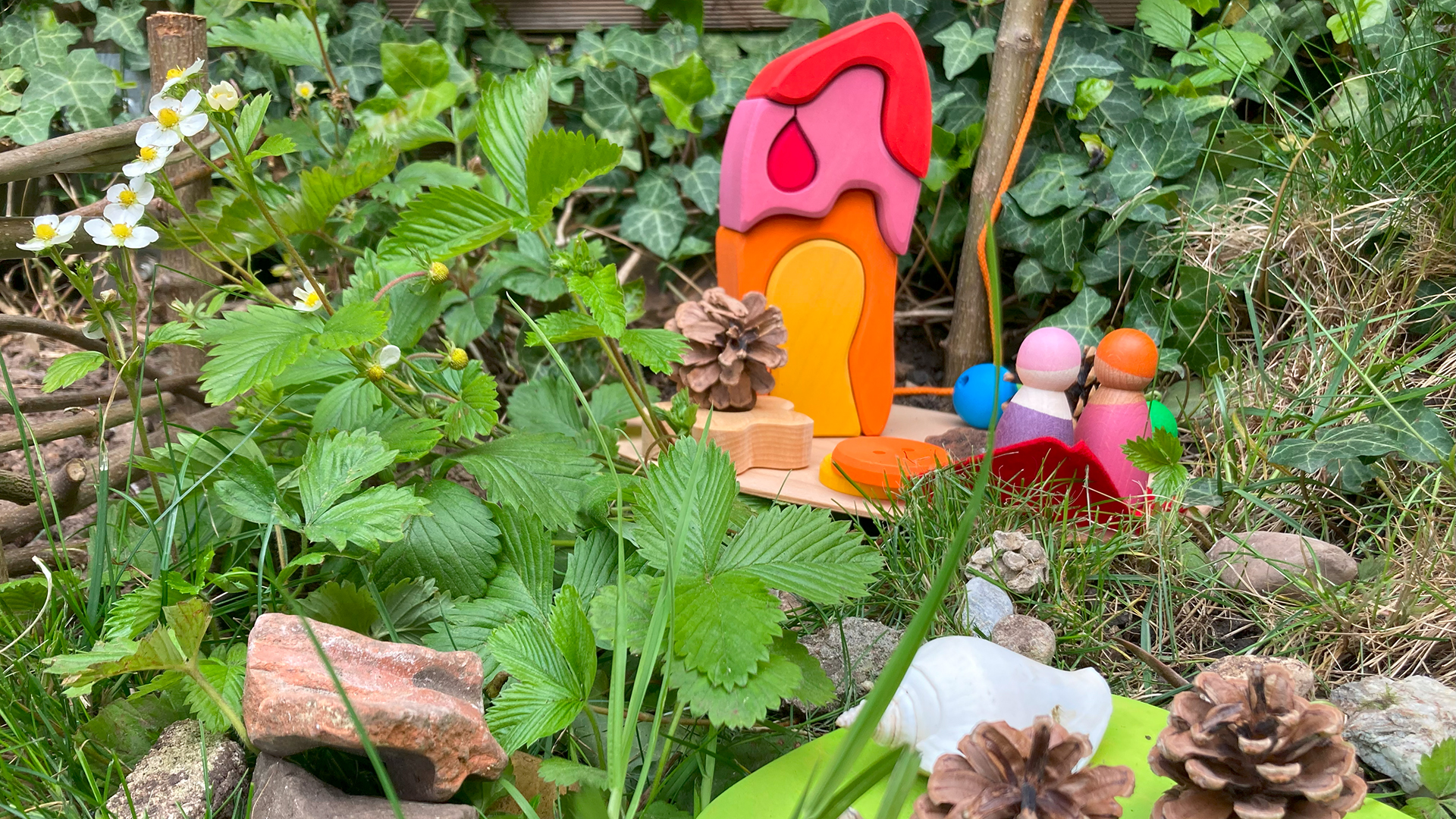 Ein kleines Spielhäuschen aus Holz steht im Gras und ist mit Naturmaterialien geschmückt.