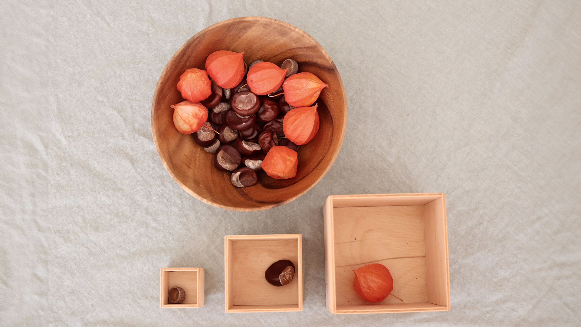 Three different sized wooden boxes and natural materials in three sizes on a table.