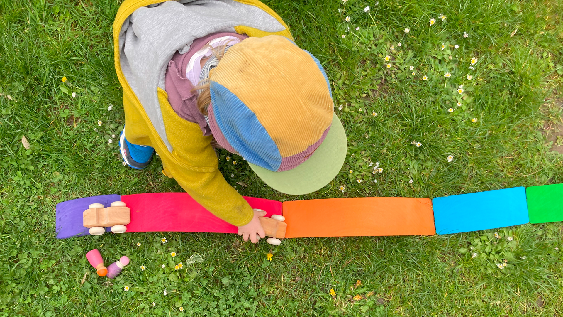 A child plays with wooden play cars on a meadow