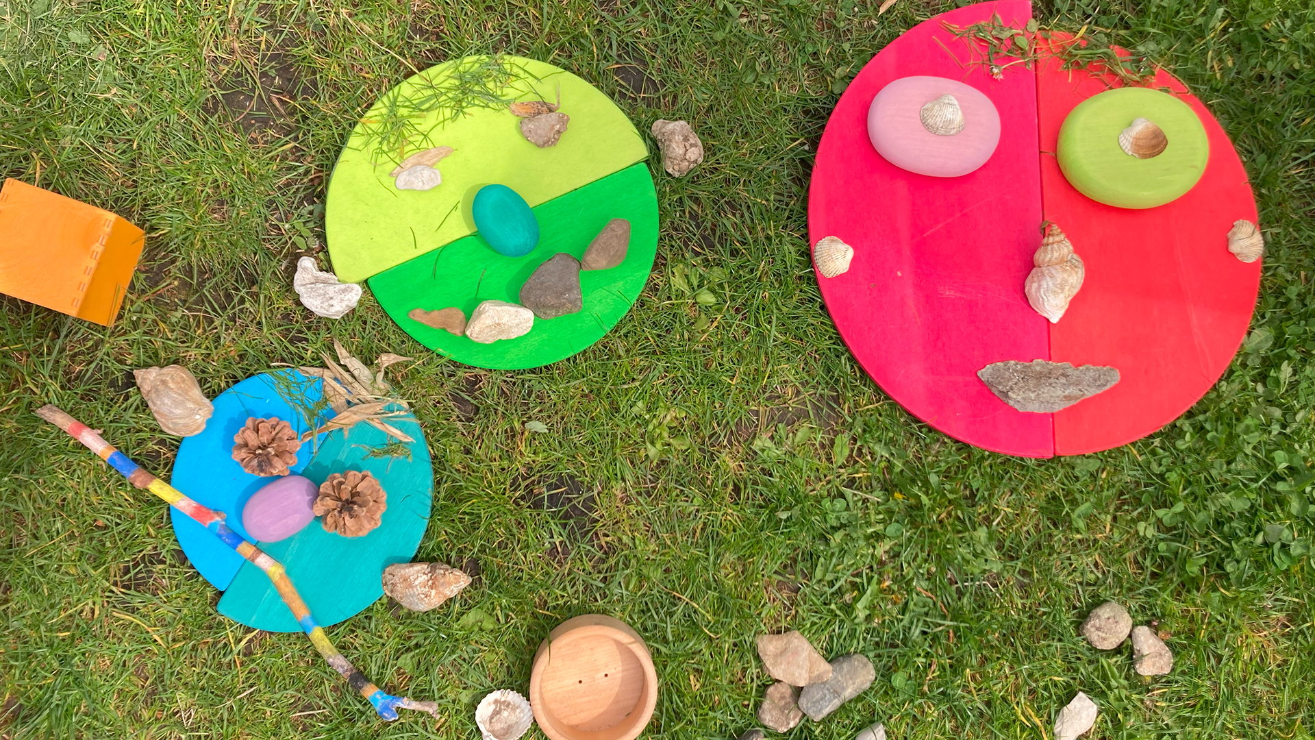 Funny faces made of wooden toys and natural materials lie on the meadow.