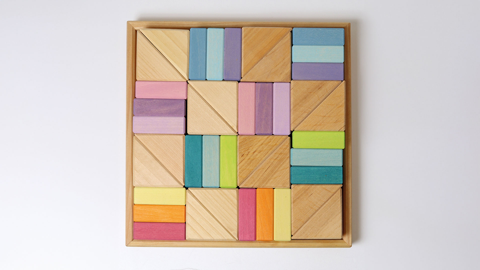 Holzrahmen mit pastellfarbenen und naturfarbenen Bausteinen in den Formen Dreieck und Rechteck.