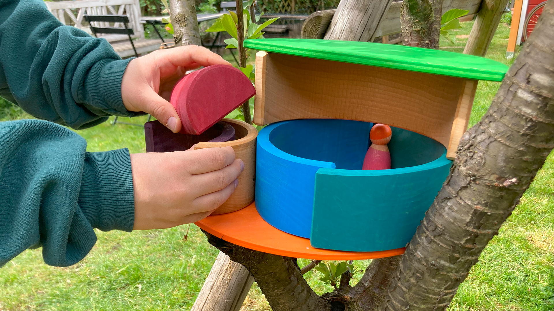 A tiny tree house is built by a childs hands in a real tree with wooden toys.