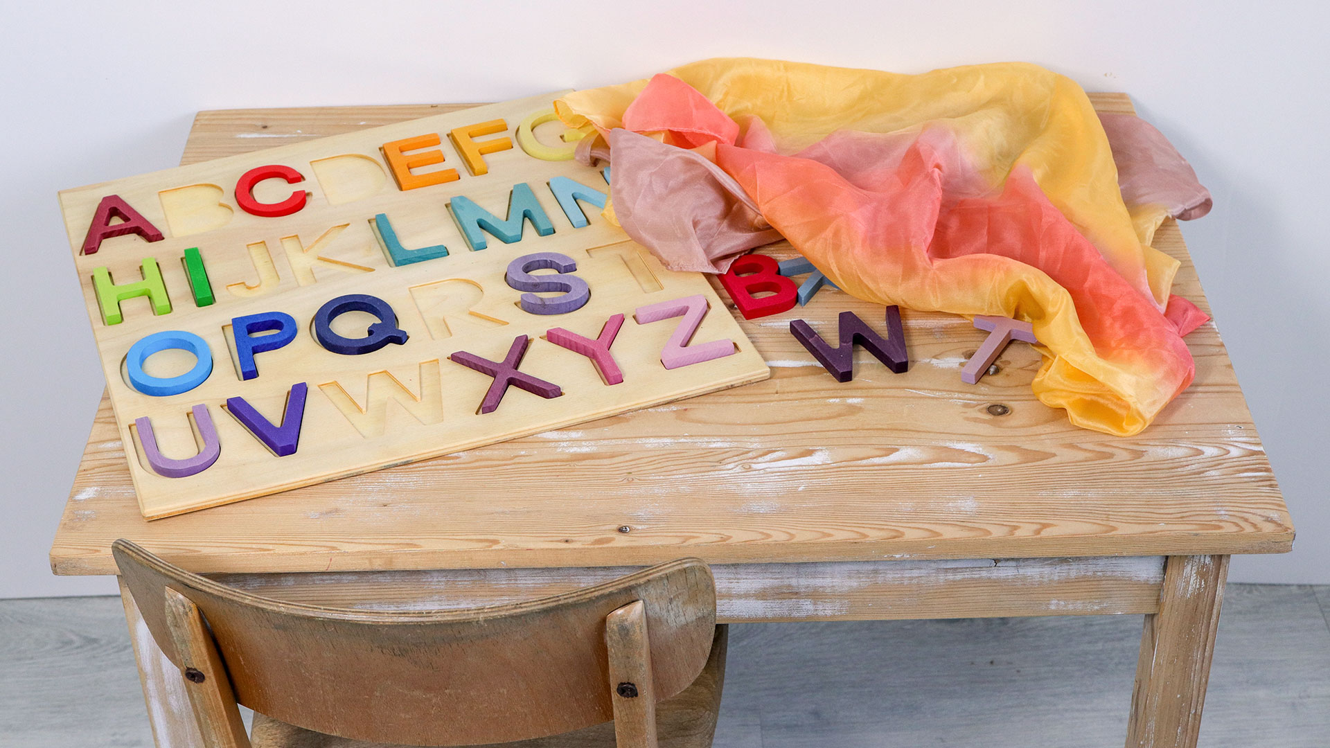 Holzbuchstaben liegen auf einem Tisch und sind zur Hälfte von einem Seidentuch bedeckt.