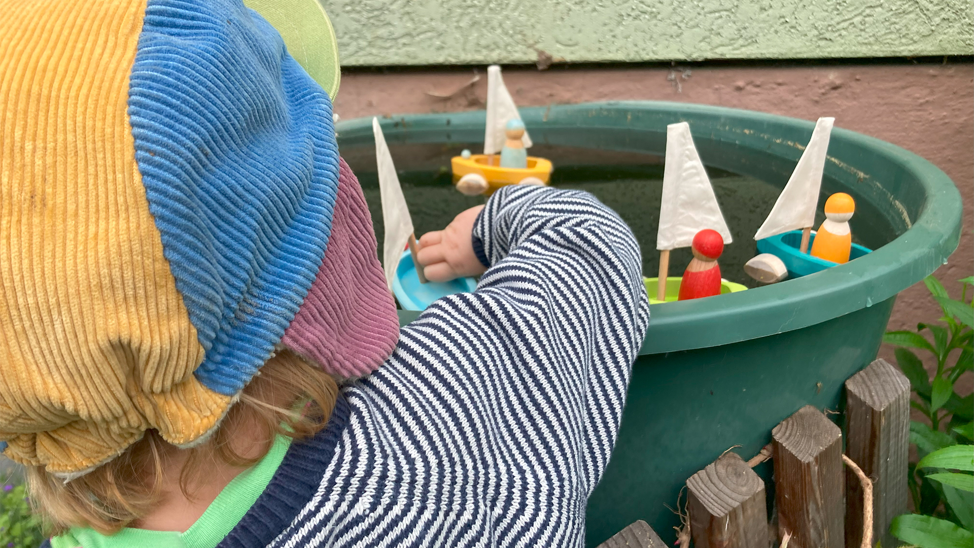 Little sailing boats of wood are swimming in a rain barrel by the hands of a child.