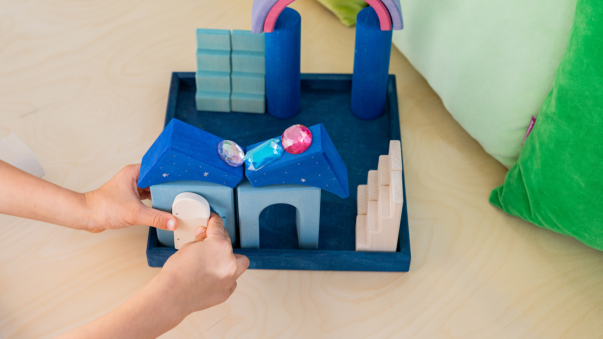 A castle built out of wooden building blocks with a child's hands