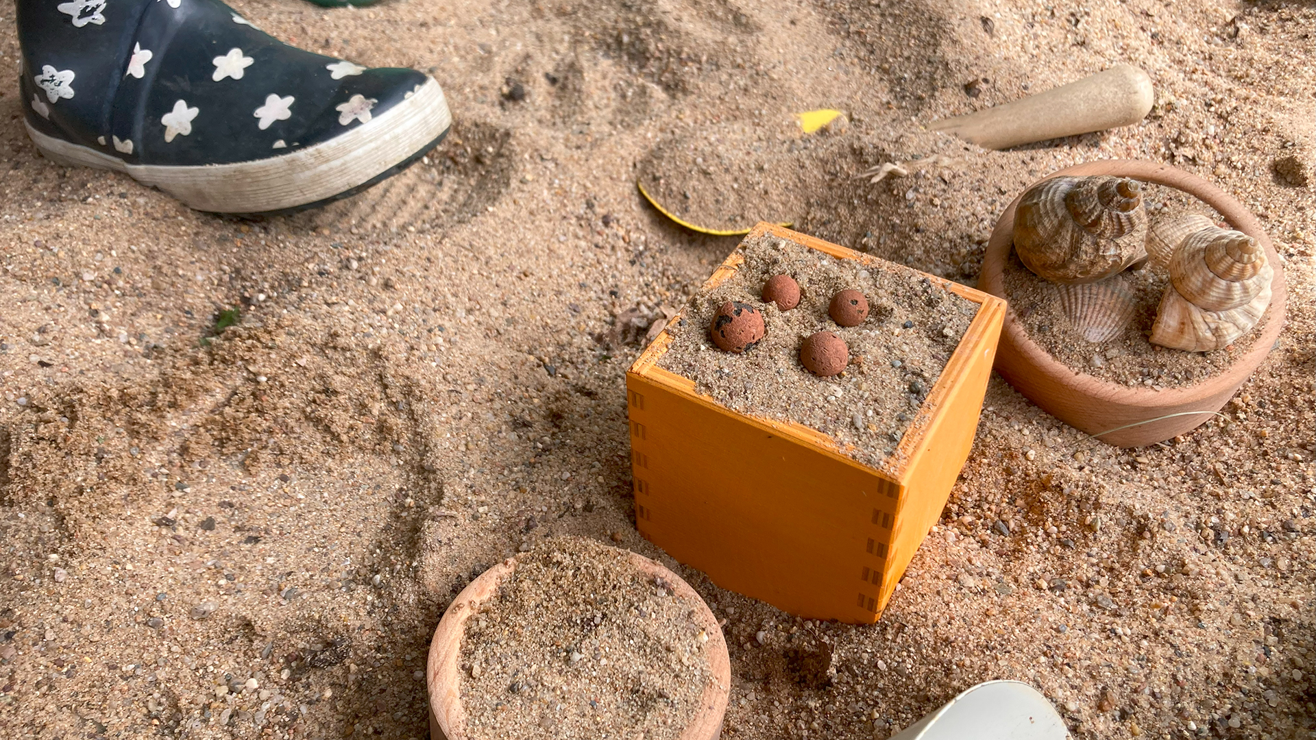 Holzschälchen sind gefüllt mit Sand und kleinen Steinchen und Muscheln.