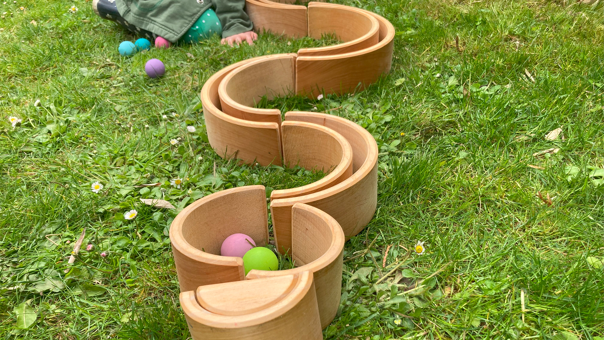 A ball run made of wooden toys stands in the meadow and a child plays with it.
